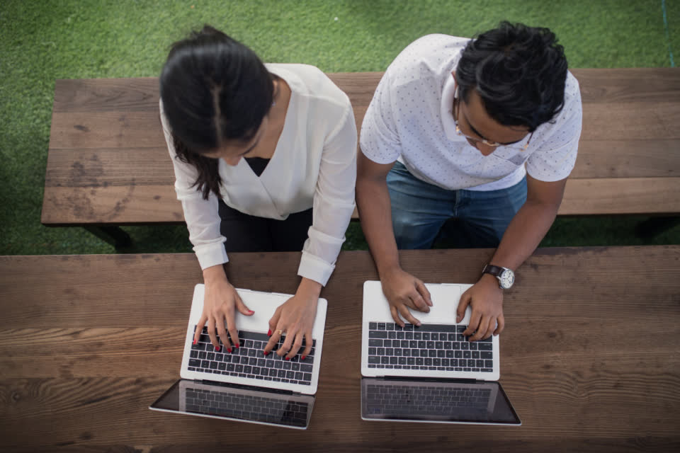Two developers typing on laptops at an outdoor table